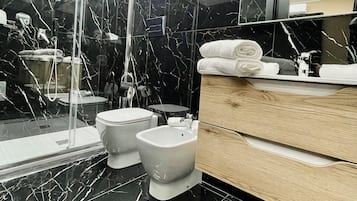 Ein modernes Badezimmer mit schwarzem Marmorboden, einer Duschkabine aus Glas, einer Toilette, einem Bidet und einem hölzernen Waschtisch mit Spiegel.