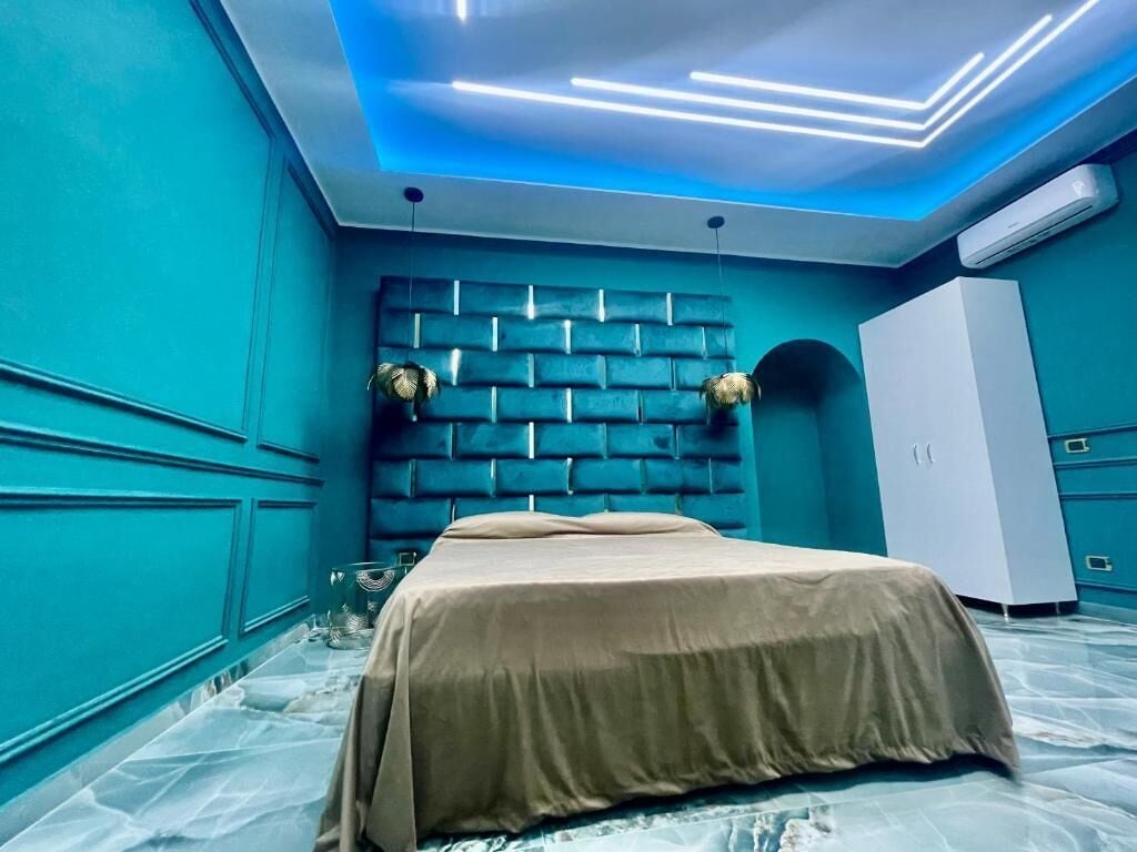 Ein Zimmer mit einem Bett, einem Wandpaneel als Kopfteil, einem Kleiderschrank und einer Decke mit LED-Beleuchtung.