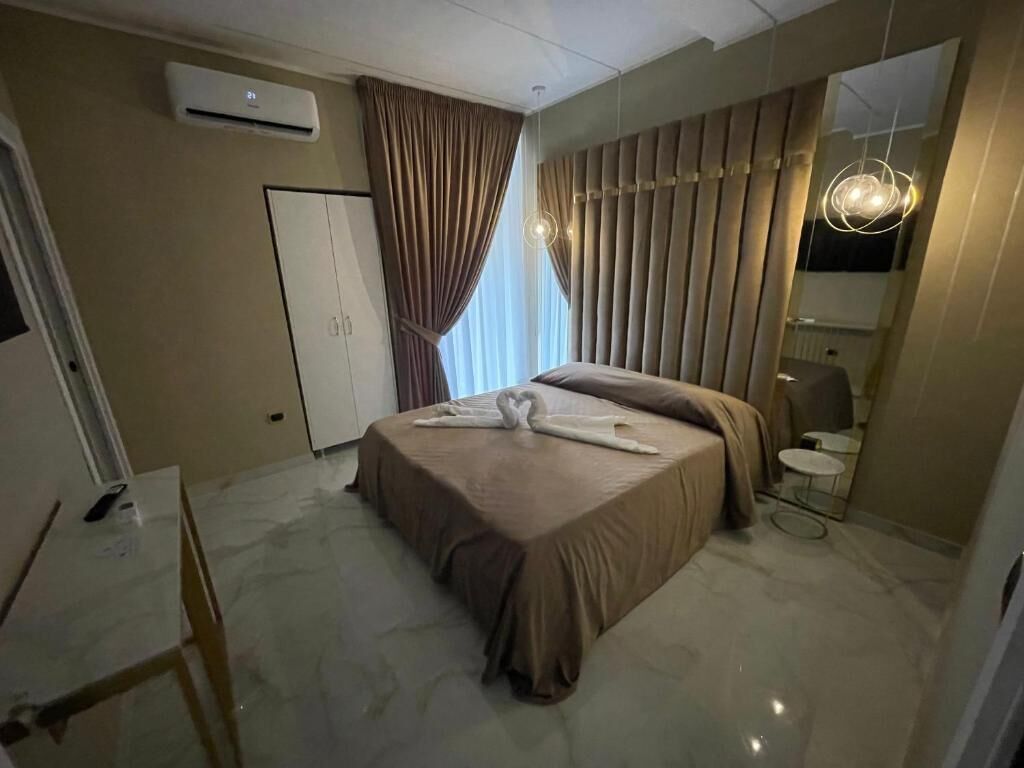 A hotel room with a bed, a desk, a mirror, and an air conditioning unit.