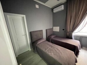A room with two beds, a door, an air conditioning unit, and a window with curtains. - Al Binario di Napoli (Naples)