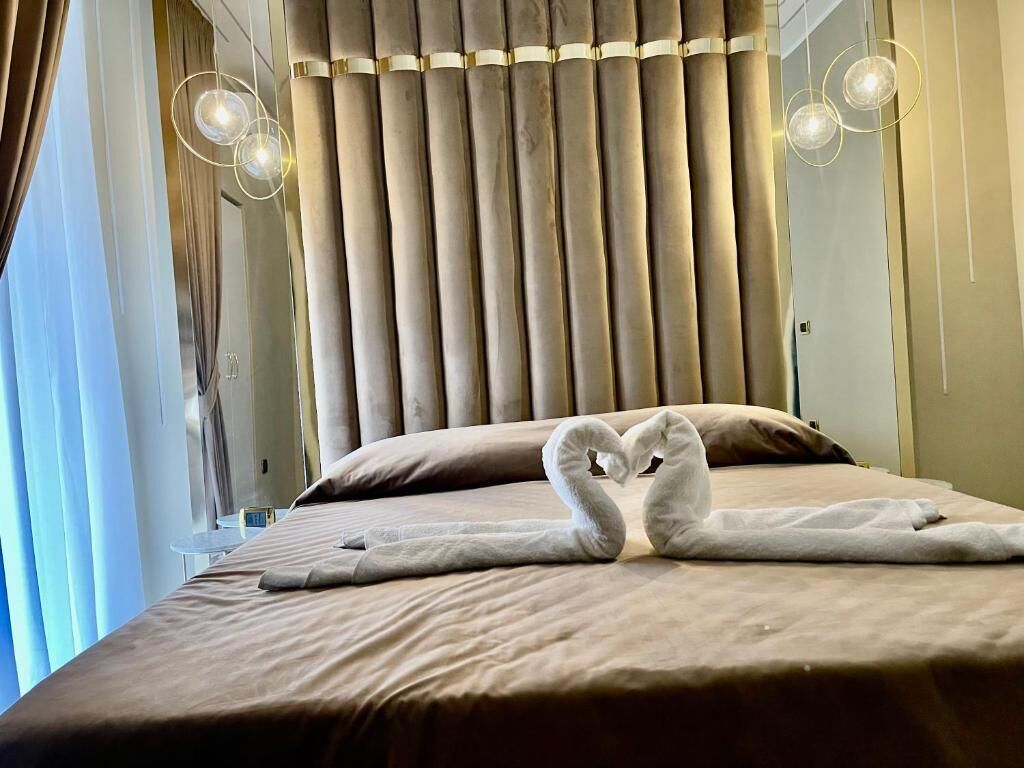 A hotel room with a bed, curtains, and a wall-mounted light fixture.
