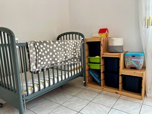 Ein Babybett mit gepunkteter Decke, eine Holz-Aufbewahrungseinheit mit Boxen und ein kleines Hausmodell.