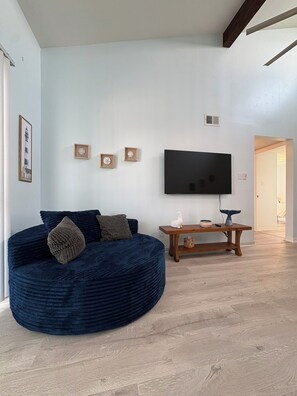 Ein Wohnzimmer mit einem großen, dunkelblauen Sofa, einem an der Wand montierten Flachbildfernseher und einem Holztisch.