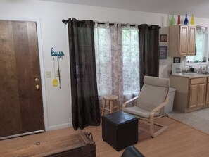 Un salon avec une porte en bois, une chaise, un petit tabouret et un pouf noir.