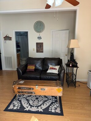 A living room with a leather sofa, a clock, a lamp, and a suitcase on a rug. - Black Bear Ridge  (Bryson City)