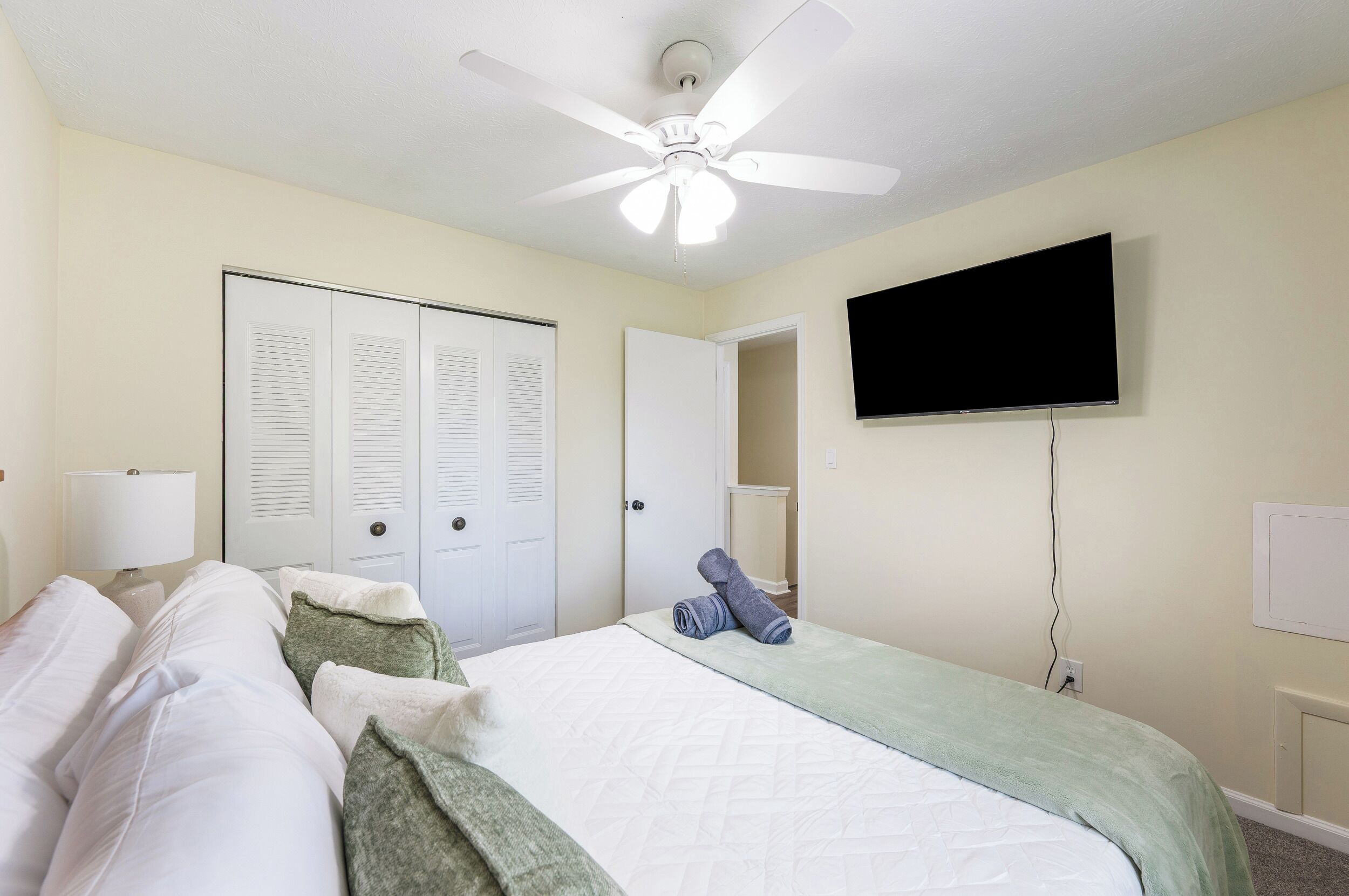 Une chambre d’hôtel avec un lit, un ventilateur de plafond, une télévision et une porte dotée de volets à persiennes.