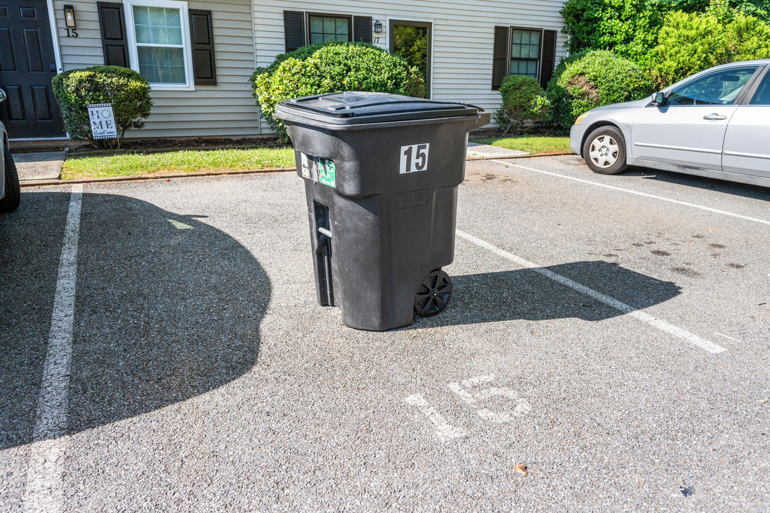 A black trash bin with the number 15 on it, placed on a parking lot.