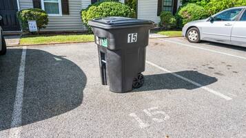 A black trash bin with the number 15 on it, placed on a parking lot.