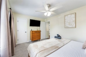 Un dormitorio con cama, cómoda, ventilador de techo, televisor de pantalla plana y una obra de arte floral enmarcada en la pared.