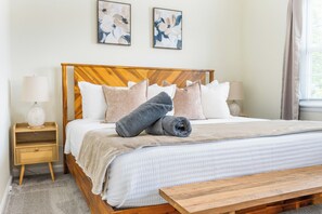 A neatly made bed with a wooden headboard, two bedside lamps, a bedside table with a lamp, and a window with curtains. - Luxury 2BR l 8 min to Liberty University l King + Queen Bedrooms  (Lynchburg)