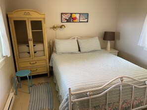 A bedroom with a bed, a wardrobe, a bedside table with a lamp, a small stool, and a rug. - Hilltop Haven, Stunning Lake Michigan Views (Muskegon)
