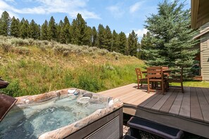 A hot tub on a wooden deck with a table and chairs, surrounded by a forested hillside. - Big Sky Escape! 5 minute walk from Town Center! (Big Sky)