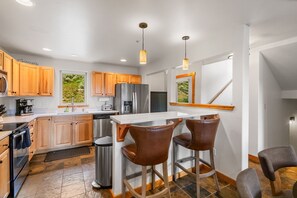 A modern kitchen with wooden cabinets, stainless steel appliances, and a bar area with stools. - Big Sky Escape! 5 minute walk from Town Center! (Big Sky)