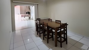 Een eetgedeelte met een houten tafel en stoelen, een betegelde vloer en uitzicht op een keuken.