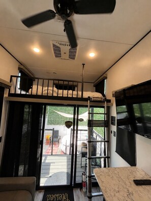 A modern interior with a ceiling fan, a bunk bed, a dining area with a table and chairs, and a sliding glass door leading to an outdoor area. - Confortable RV/Near Beaches & Downtown WPB. (West Palm Beach)