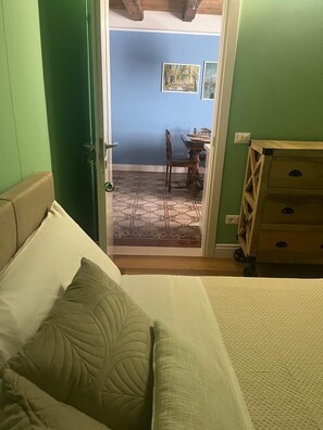 Et soveværelse med seng, kommode og en dør, der fører til en balkon med bord og stole.