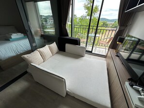 A modern bedroom with a sofa bed, a TV, and a balcony with a view of the city. - La Casita Hua Hin Premium Stay with Playstation (Tambon Hua Hin)