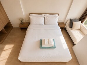 A neatly made bed with white linens, a bedside table with a vase of flowers, and a sofa with cushions. - La Casita Hua Hin Premium Stay with Playstation (Tambon Hua Hin)