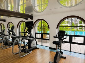 A gym with exercise equipment and large windows overlooking a swimming pool. - La Casita Hua Hin Premium Stay with Playstation (Tambon Hua Hin)