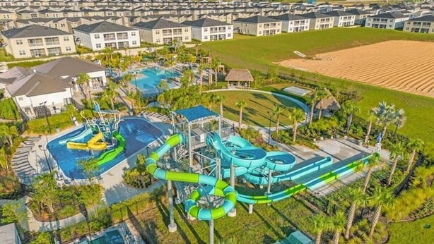 Eine Vogelperspektive zeigt ein Resort mit mehreren Schwimmbecken, Wasserrutschen und einer gepflegten Landschaft mit Palmen.
