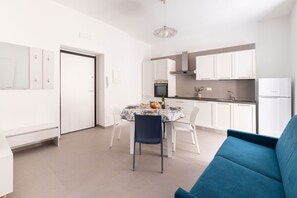 Eine moderne Küche mit weißen Schränken, einem Esstisch für vier Personen und einem blauen Sofa im Wohnbereich.