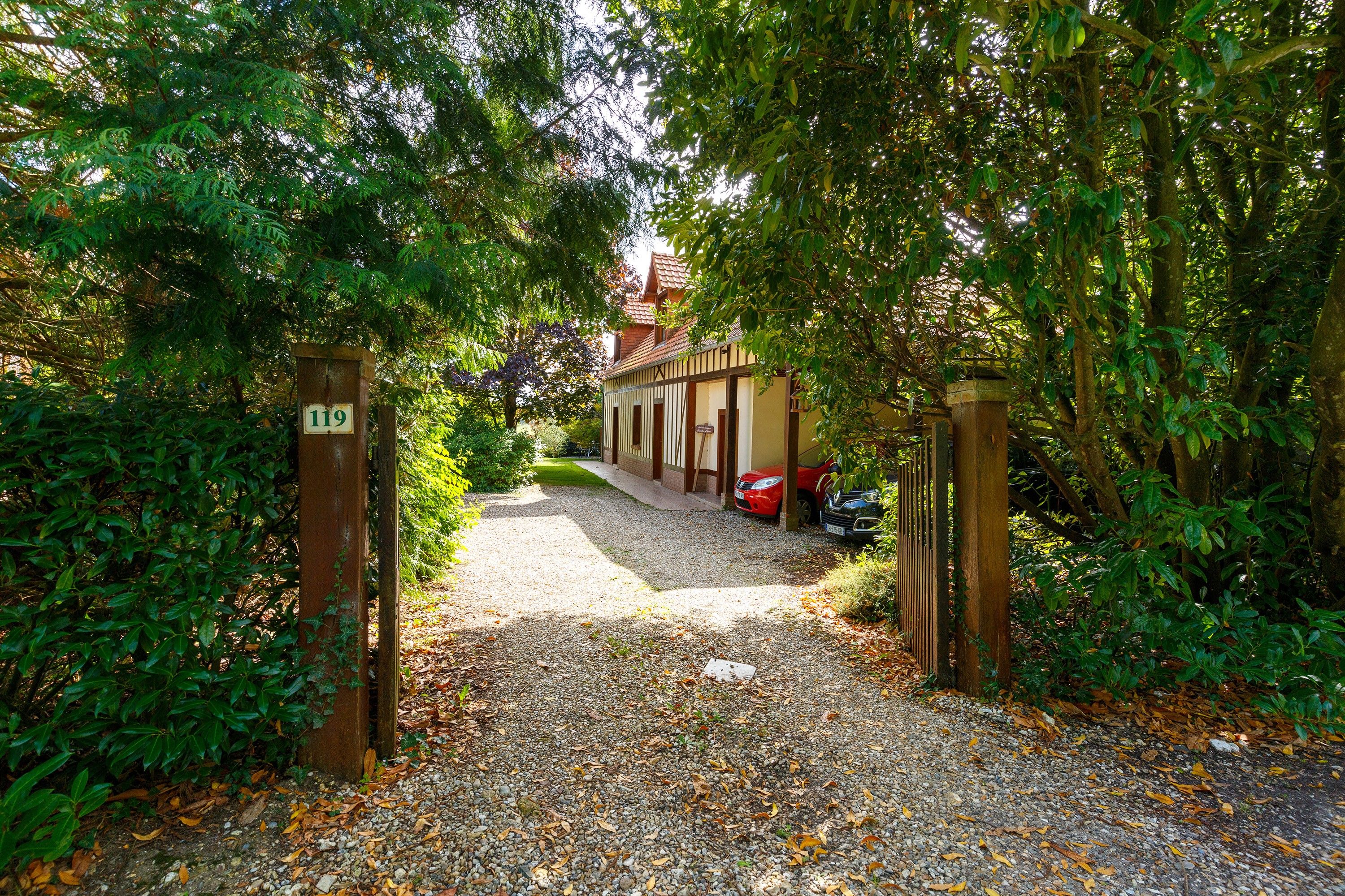 A gravel driveway leading to a building with a traditional facade, surrounded by dense foliage.