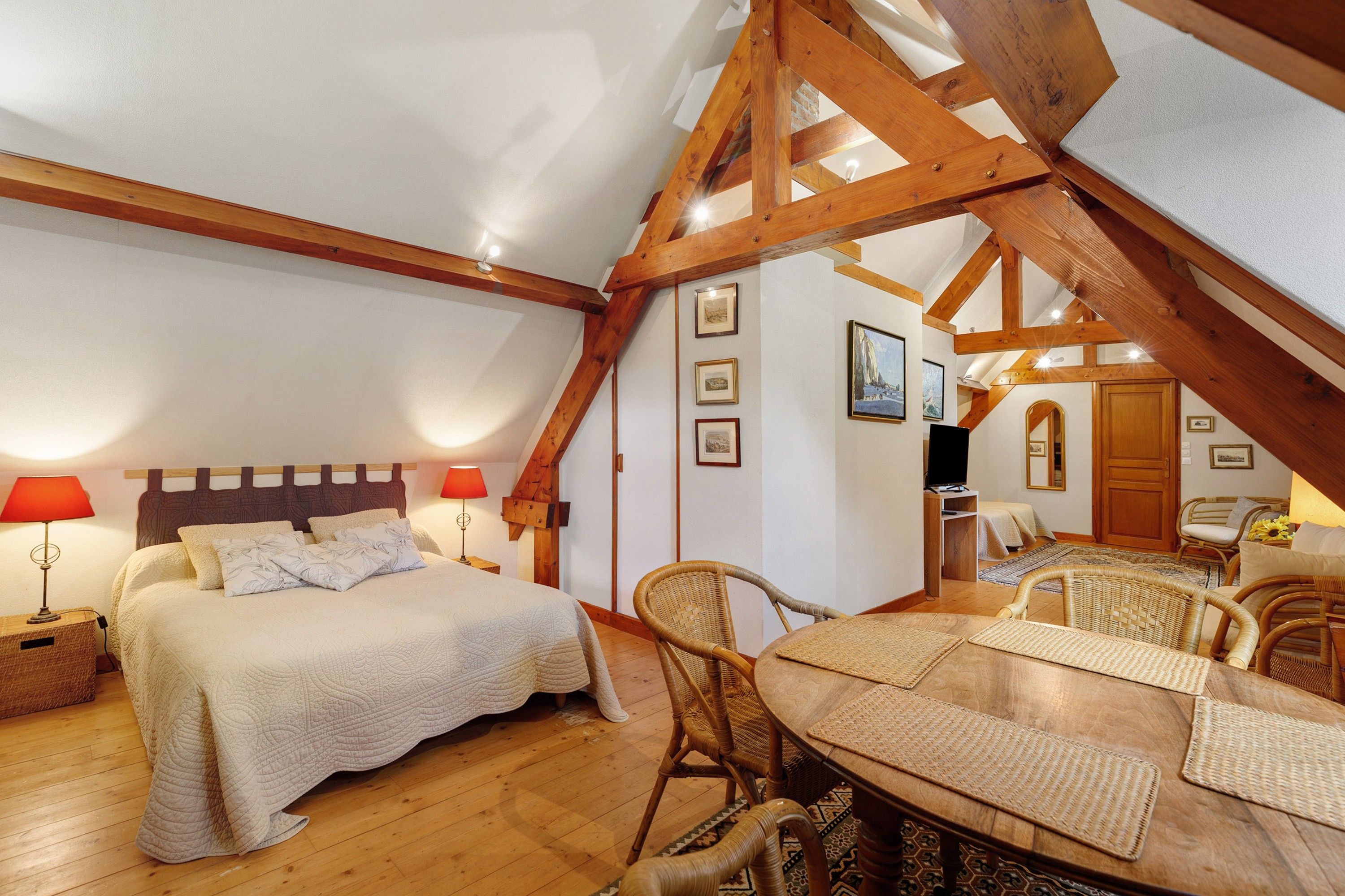 Une chambre confortable située sous les toits, avec un lit, des lampes de chevet, une table à manger avec des chaises et un téléviseur.