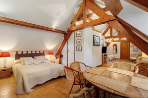 A cozy attic bedroom with a bed, bedside lamps, a dining table with chairs, and a television.