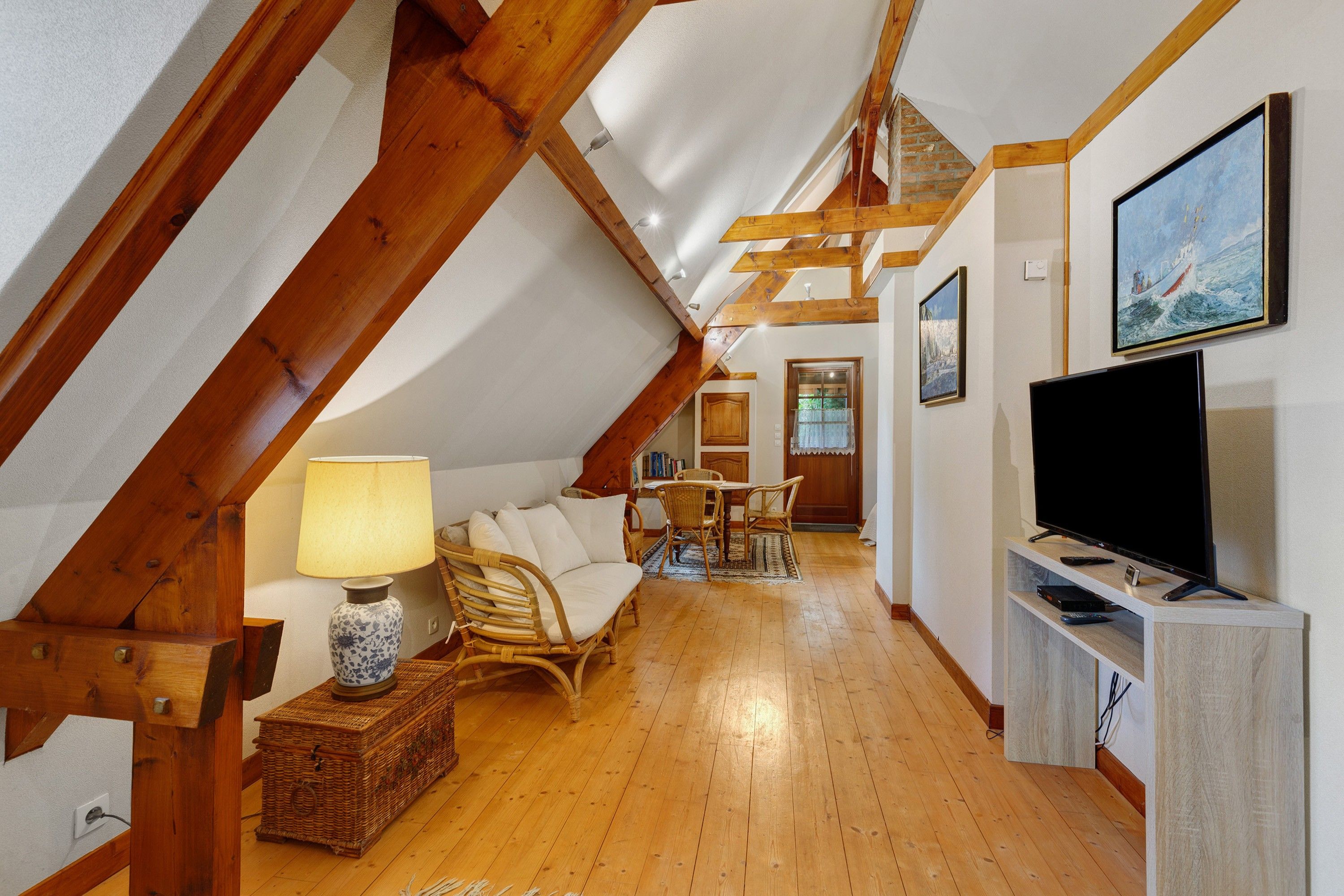 A cozy attic room with wooden beams, a television, a sofa, and a dining area.