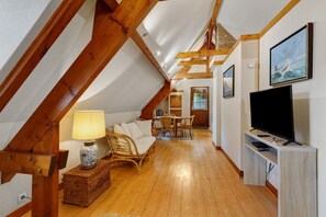 A cozy attic room with wooden beams, a television, a sofa, and a dining area. - Bed and Breakfast 'Sous Les Bruyères' with Private Terrace, Private Garden and Wi-Fi (Sainte-Marguerite-sur-Mer)