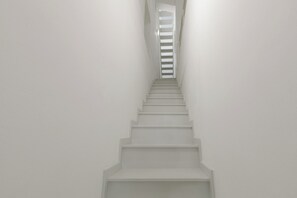Una escalera blanca y recta que asciende, con un descansillo estrecho en la parte superior.