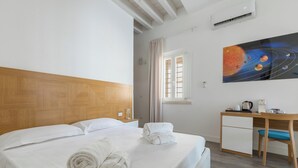 Habitación de hotel con cama, escritorio, un cuadro de planetas y ventana con cortinas.