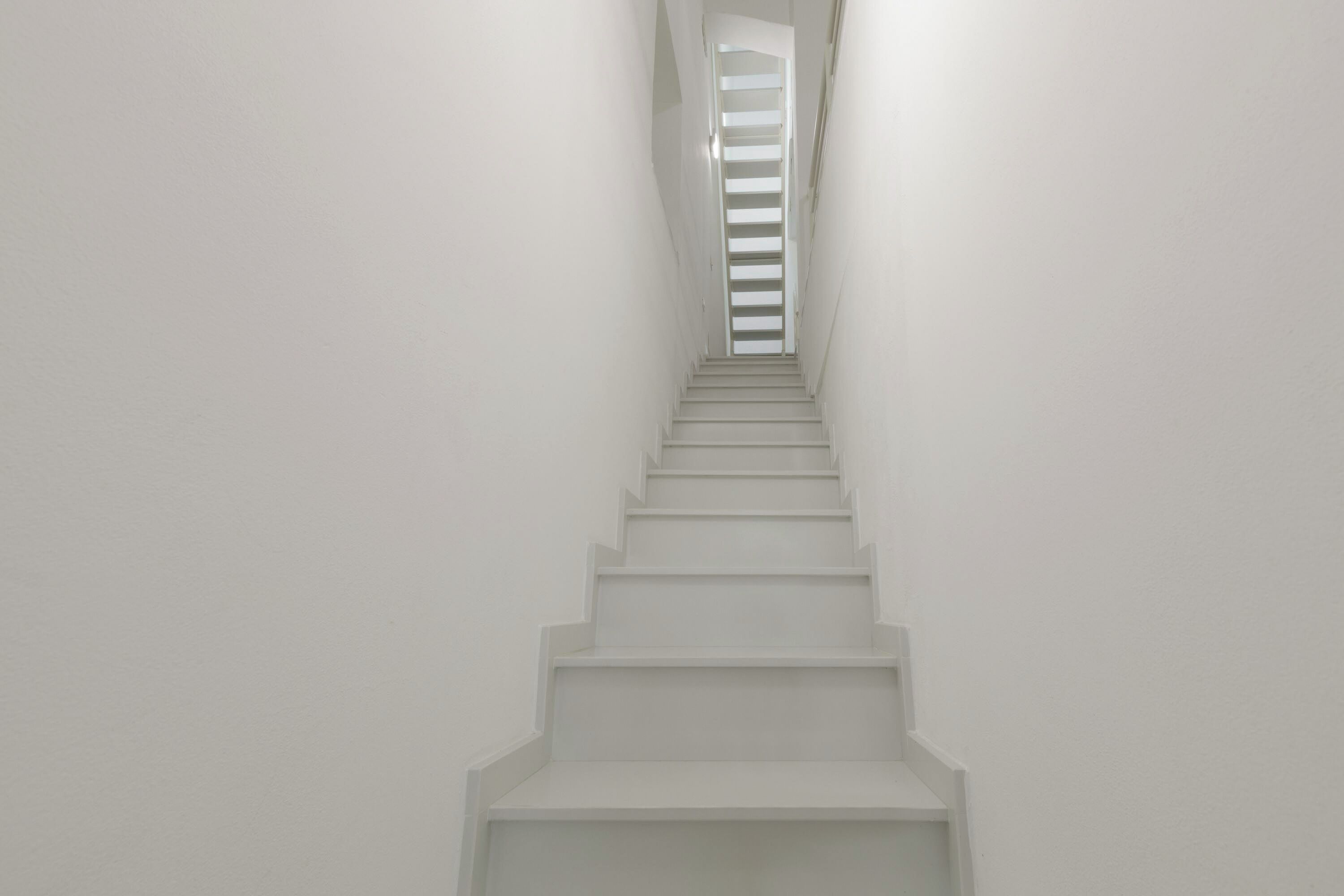 A straight, white staircase leading upwards with a narrow landing at the top.
