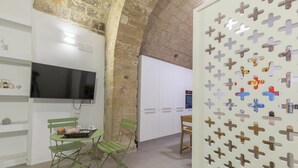 Una habitación con televisión, una mesa de comedor con sillas, una zona de cocina y un muro decorativo con formas recortadas.