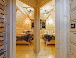 Interior de una cabaña de madera con dos camas, una ventana y una lámpara en el techo.