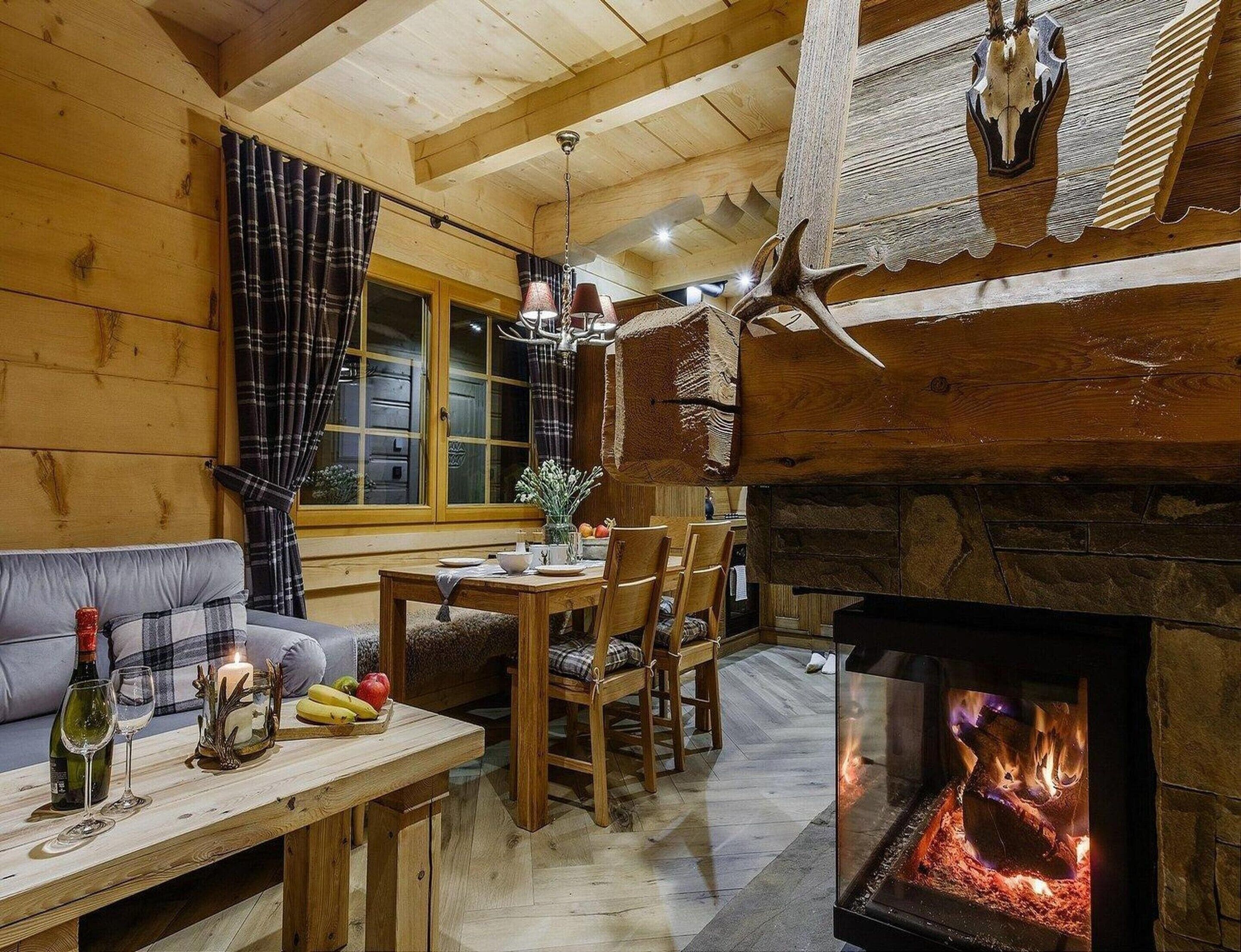 A cozy cabin interior with a stone fireplace, wooden furniture, and a plaid curtain.