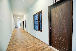 Un pasillo con piso de madera, una puerta grande de madera con picaporte circular y una ventana con persianas horizontales.