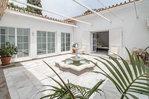 A courtyard with a fountain, potted plants, and a bed visible through an open door. - Villa Alegre - Charming Villa With Private Pool (Benahavis)