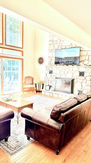 A living room with a stone fireplace, a television mounted on the wall, a leather sofa, and a dining table with chairs.