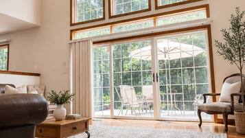 A spacious living room with a large window, a ceiling fan, and a wooden floor.