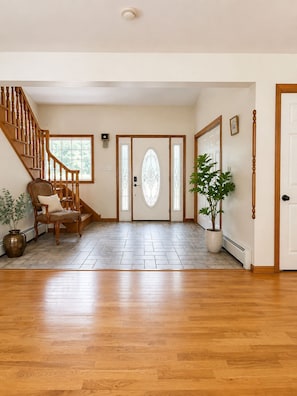 A spacious foyer with a wooden staircase, a large door with a decorative glass panel, and a potted plant.