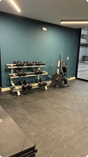 Un gimnasio con equipamiento de levantamiento de pesas, incluyendo mancuernas y barra.