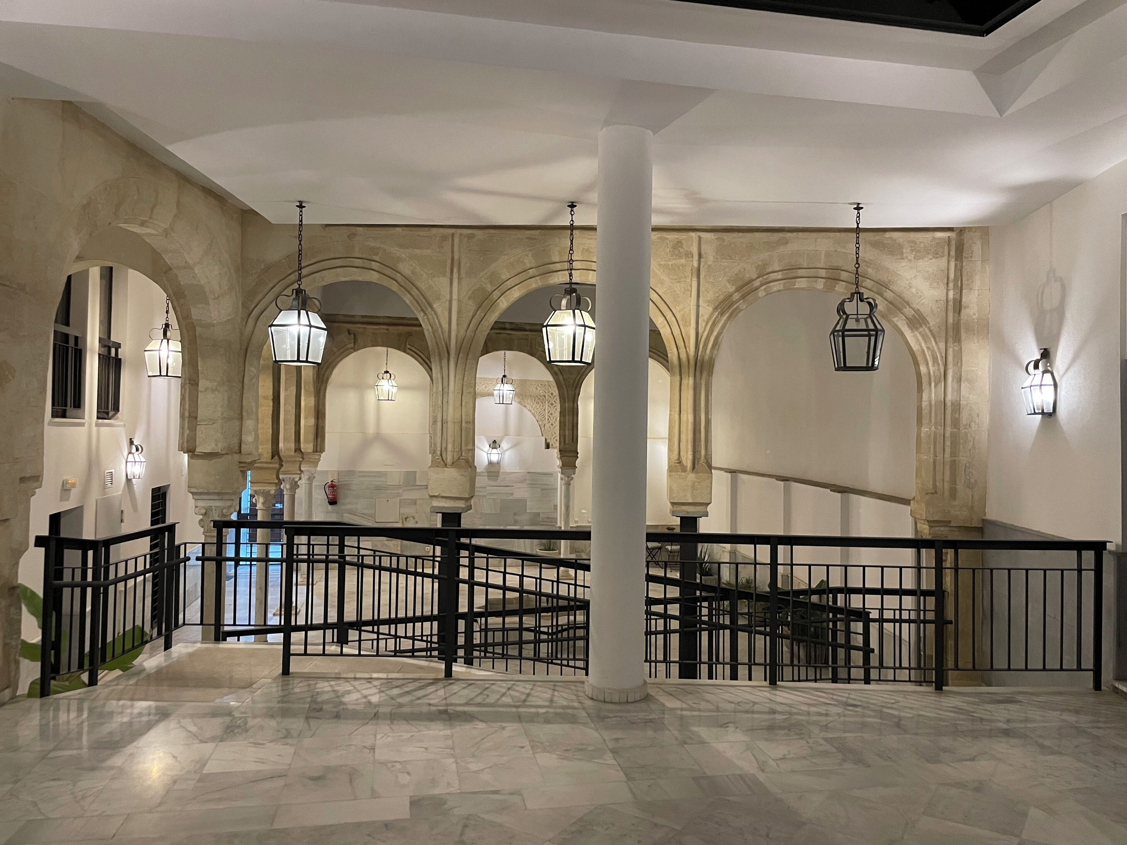 A spacious interior with high ceilings, arched columns, and hanging lantern-style lights.