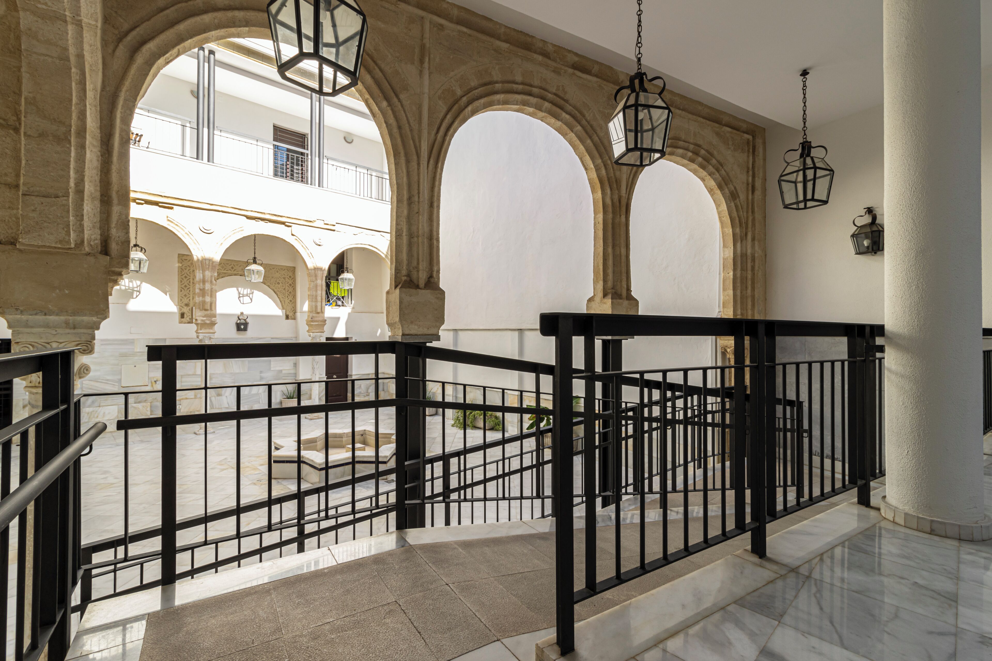 A spacious courtyard with a marble floor, black metal railing, and arches.