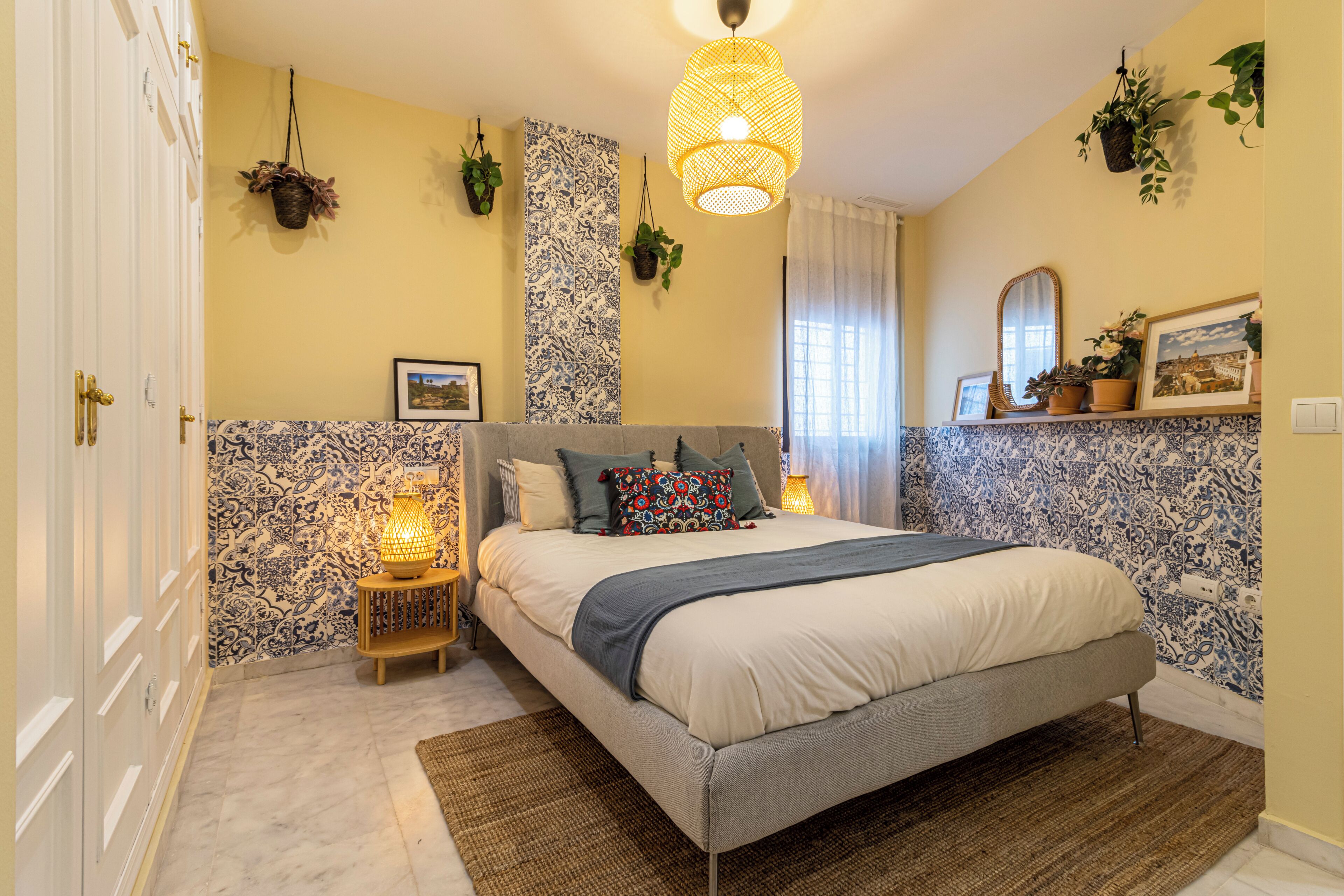 A bedroom with a bed, bedside lamps, a hanging light fixture, and wall-mounted plants.