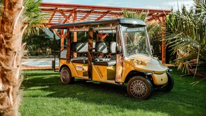 Un carrito de golf amarillo estacionado en un césped, con una pérgola roja al fondo.