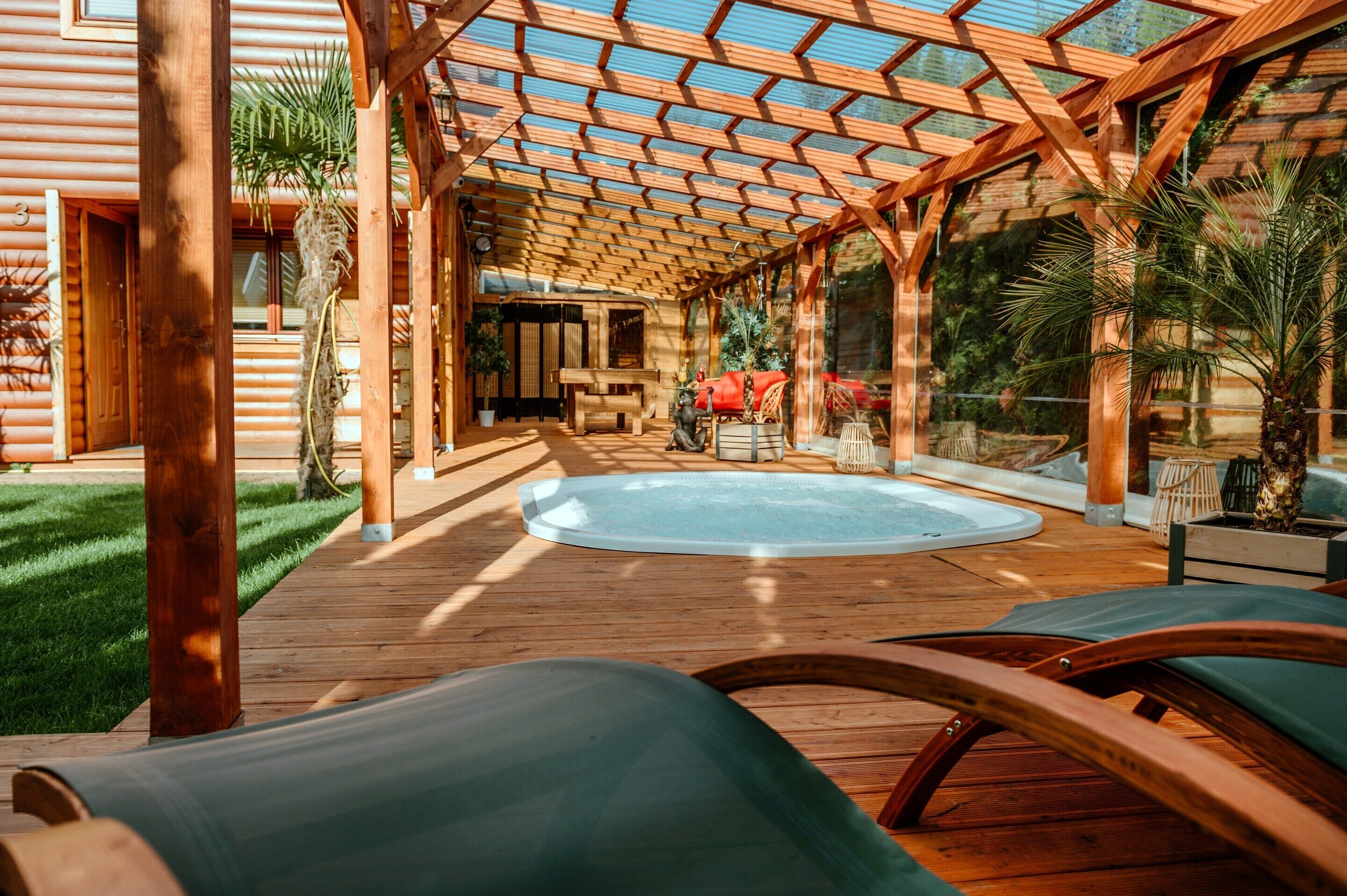 Een houten terras met een jacuzzi, lounge fauteuils en een pergola.