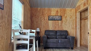 Et hyggeligt rum med træpaneler, en grå sofa, en hvid stol og et bord med en lampe.