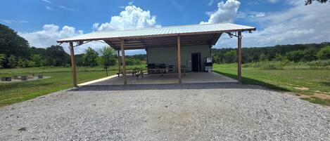 Un espacio al aire libre techado con piso de grava, mesas de picnic y un edificio con techo de metal.