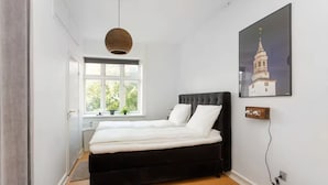Ein Schlafzimmer mit einem Bett, einem Fenster, einer Wandleuchte und einem gerahmten Bild.